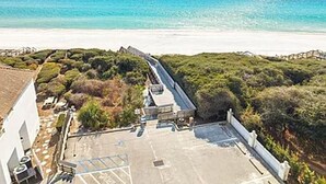Luchtbeeld van een kustbezit met een verhard gebied, een wit gebouw en een strand op de achtergrond.