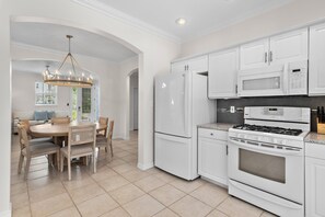 A modern kitchen with white cabinetry, a built-in oven, a microwave, and a dining area with a wooden table and chairs. - Blue Chip Escape (Santa Rosa Beach)