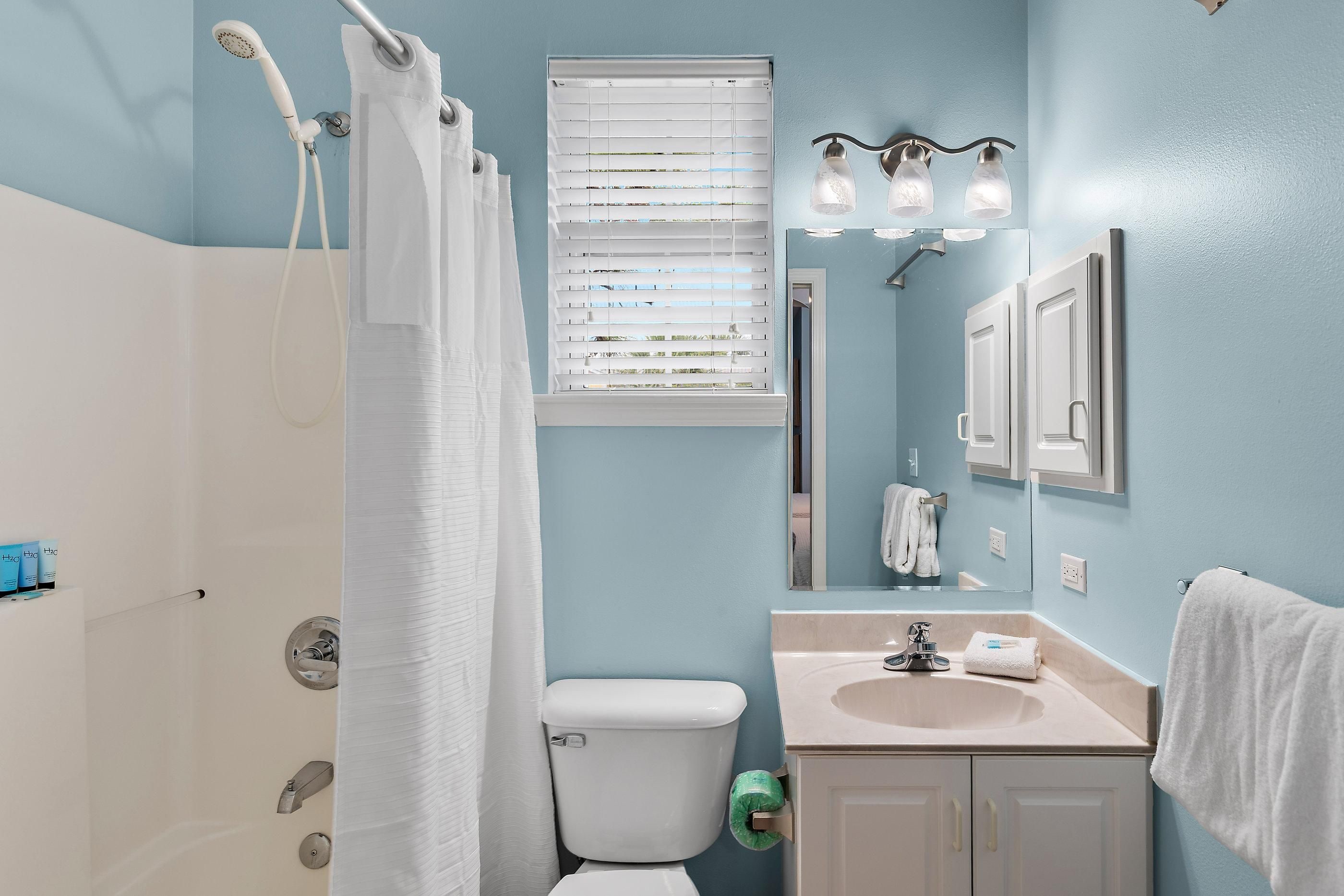 A bathroom with a shower, toilet, sink, and a mirror.