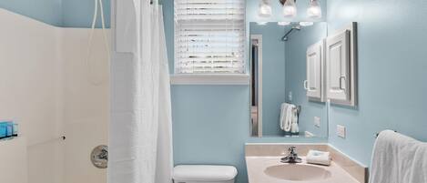 A bathroom with a shower, toilet, sink, and a mirror.