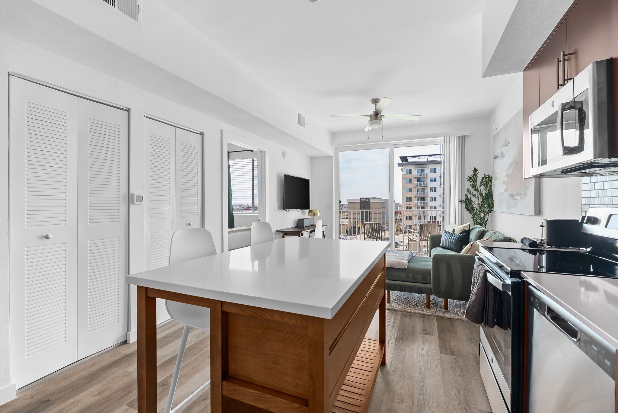 A modern kitchen with a dining area, a TV, and a balcony with a view of the city.
