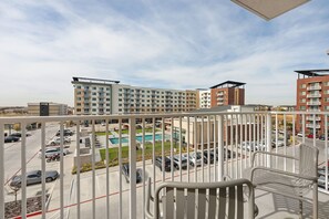 A balcony with a view of a swimming pool, parking lot, and multi-story buildings. - Lodgeur Denton (Denton)