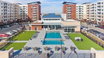 A modern apartment complex with a central swimming pool, outdoor seating, and a parking area.