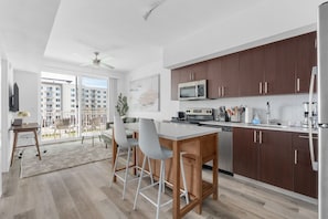 A modern kitchen with wooden cabinets, a microwave, and a dishwasher. There is a dining area with a table and chairs. - Lodgeur Denton (Denton)