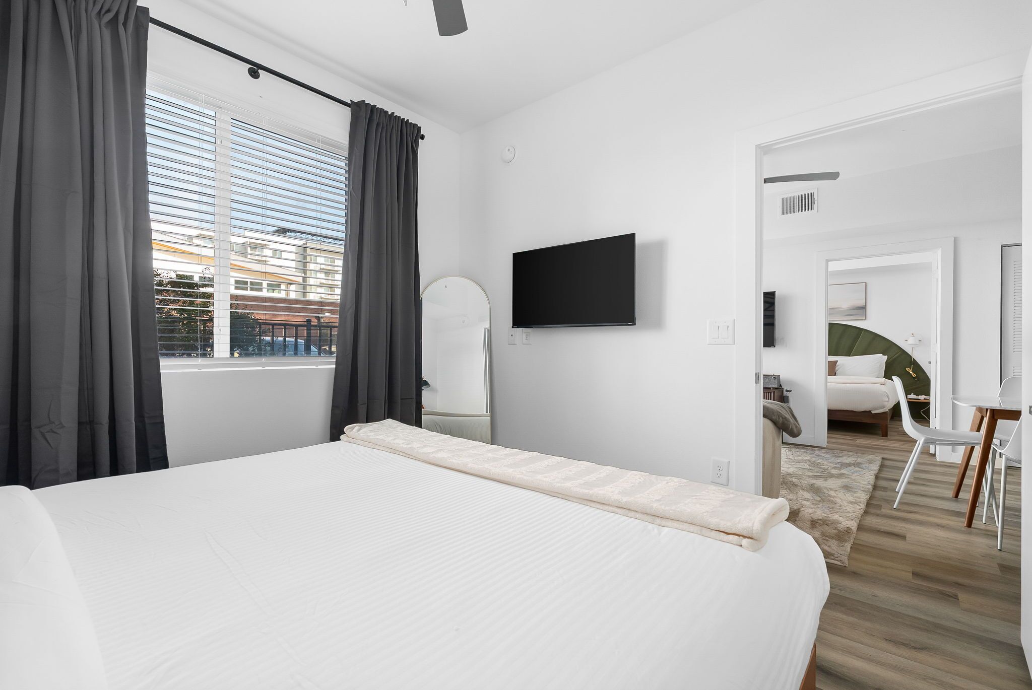 A modern hotel room with a large bed, a flat-screen TV, and a view of the city through the window.