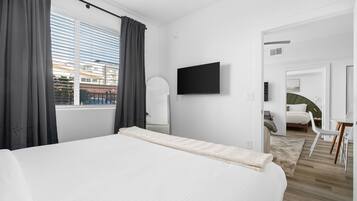 A modern hotel room with a large bed, a flat-screen TV, and a view of the city through the window.