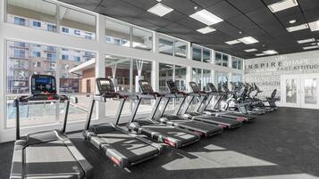 Un gimnasio con cintas de correr alineadas, amplias ventanas y vistas a edificios.