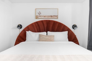 A bed with a curved headboard, white bedding, and a single decorative pillow. - Lodgeur Denton (Denton)