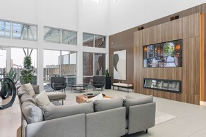 Um interior moderno com um sofá modular cinza, uma mesa de centro e uma TV fixada numa parede de madeira.