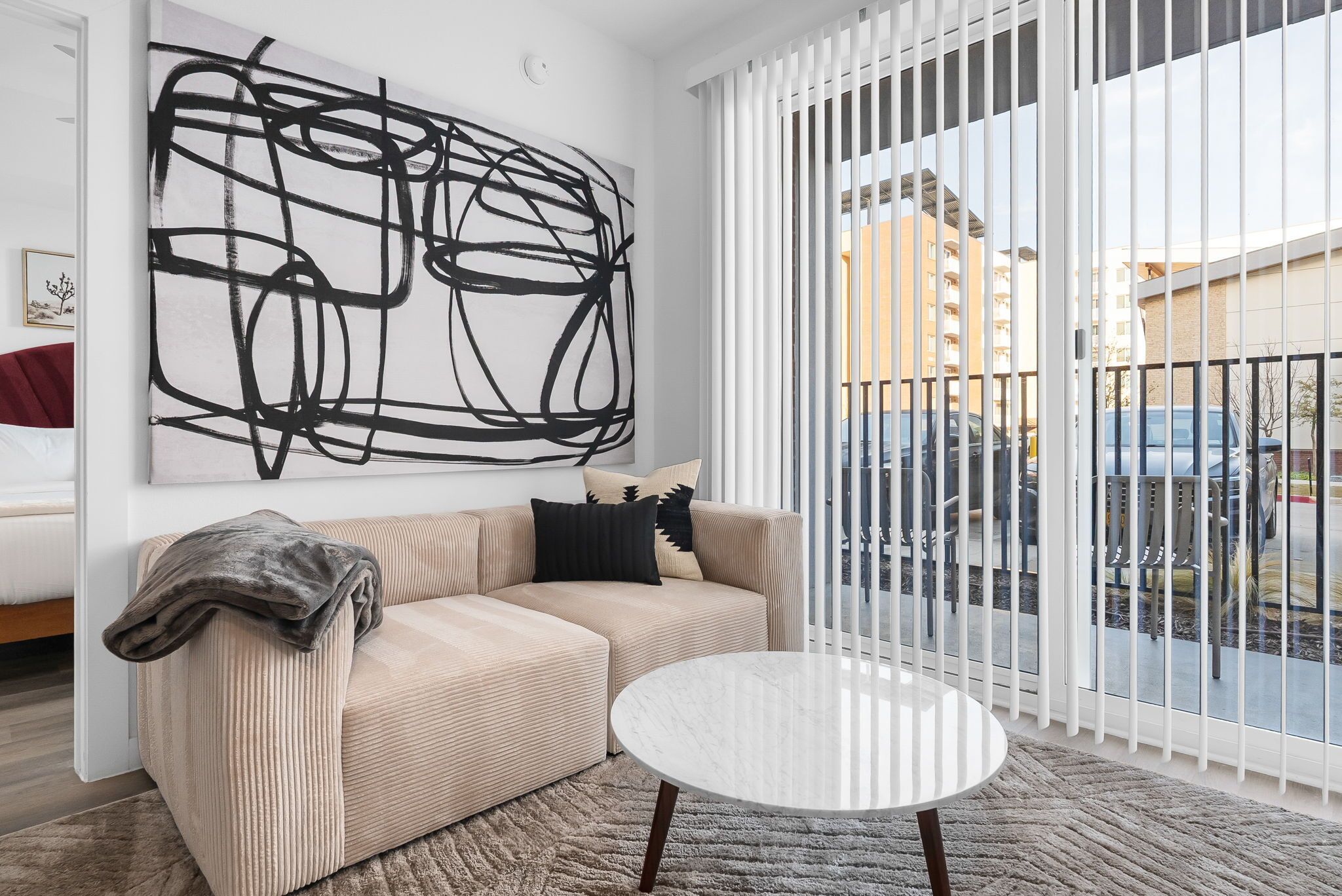 A modern living room with a beige sofa, a round white coffee table, and a large abstract painting on the wall.