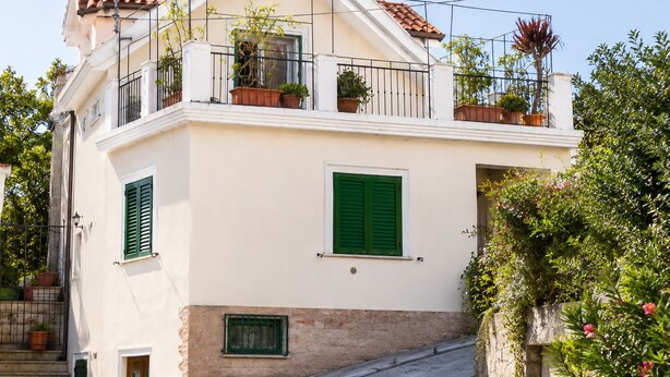 Ein zweistöckiges Gebäude mit einem Balkon, grünen Fensterläden und Kübelpflanzen.