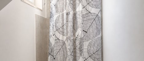 A bathroom with a shower curtain featuring a leaf pattern, a tiled shower area, and a window above the shower.