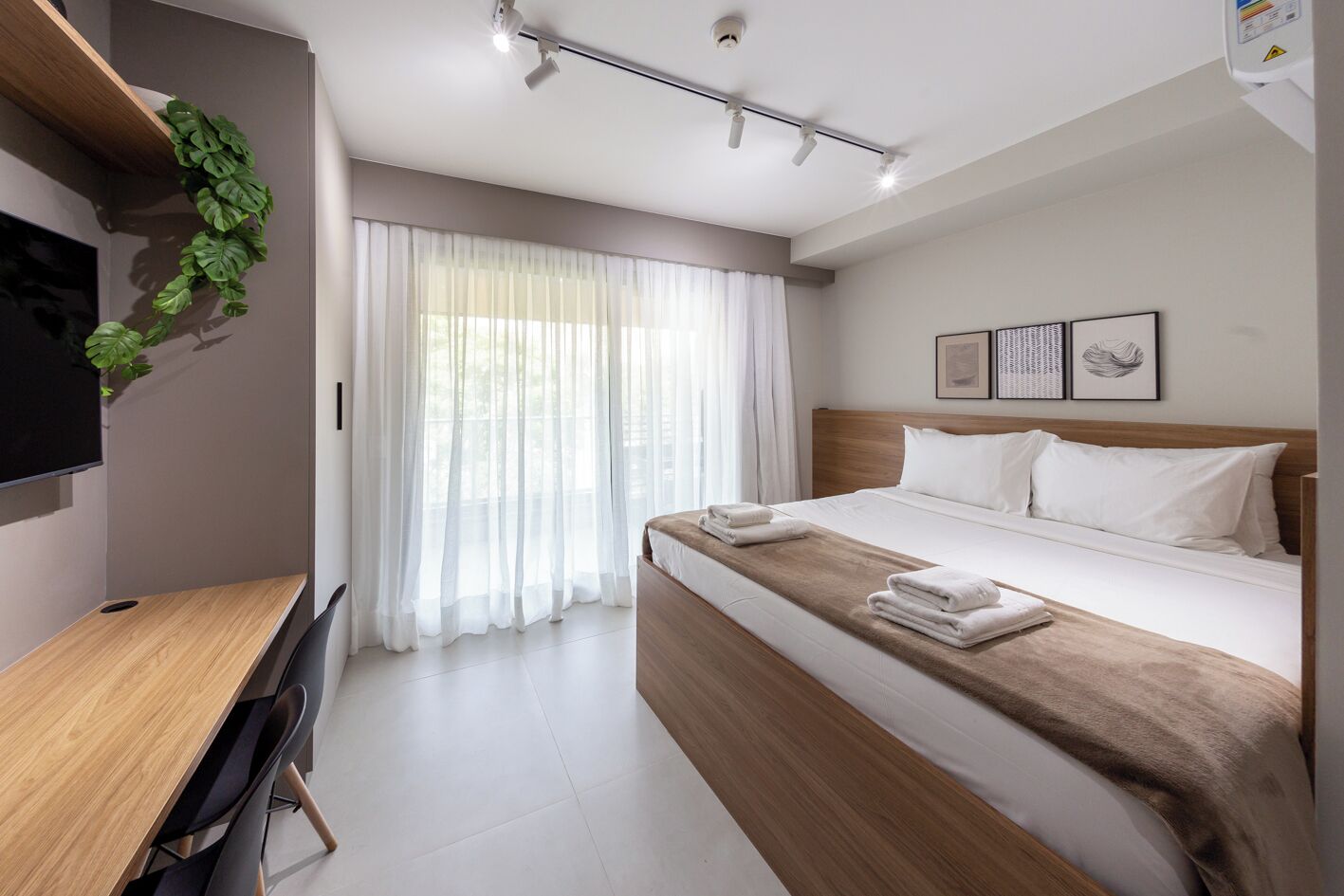 A hotel room with a bed, a desk, a TV, and a window with curtains.