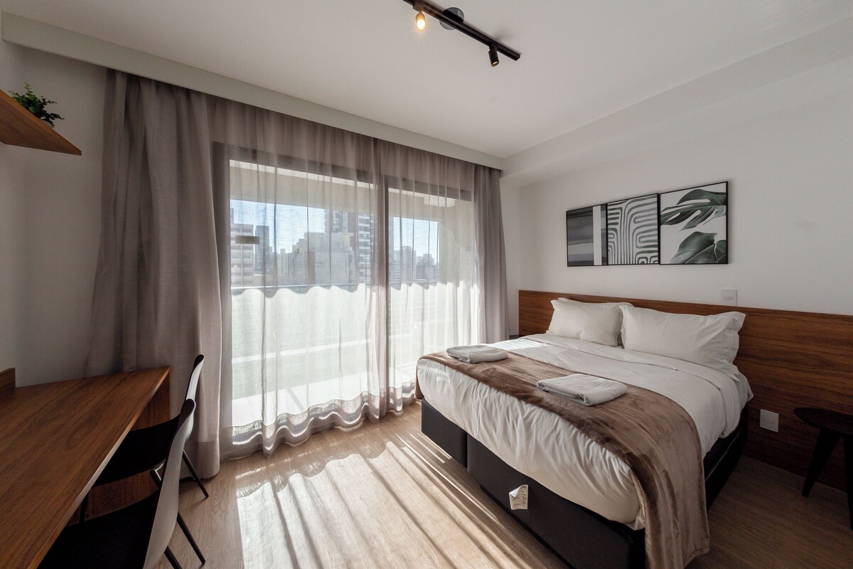 A hotel room with a bed, a desk, a chair, and a window with curtains.