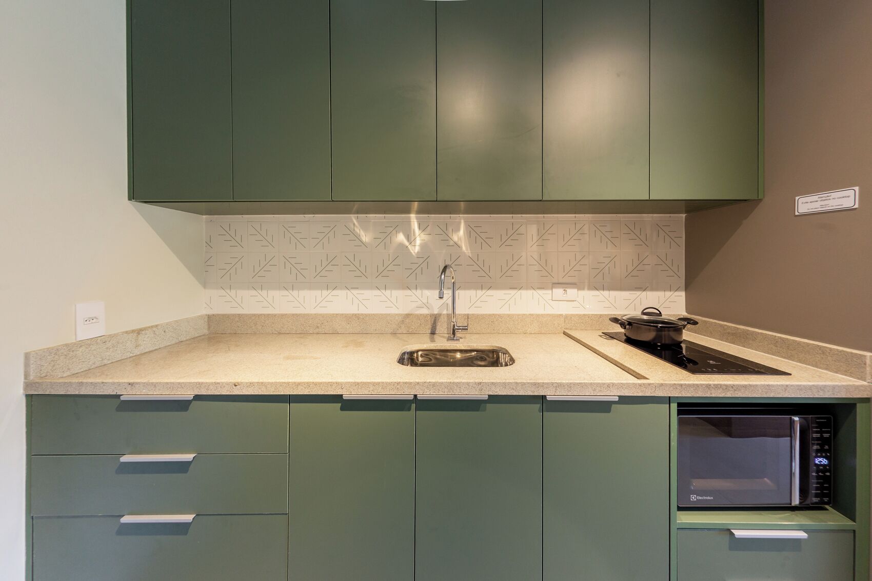 A kitchen with green cabinets, a stainless steel sink, a microwave, and a stove.