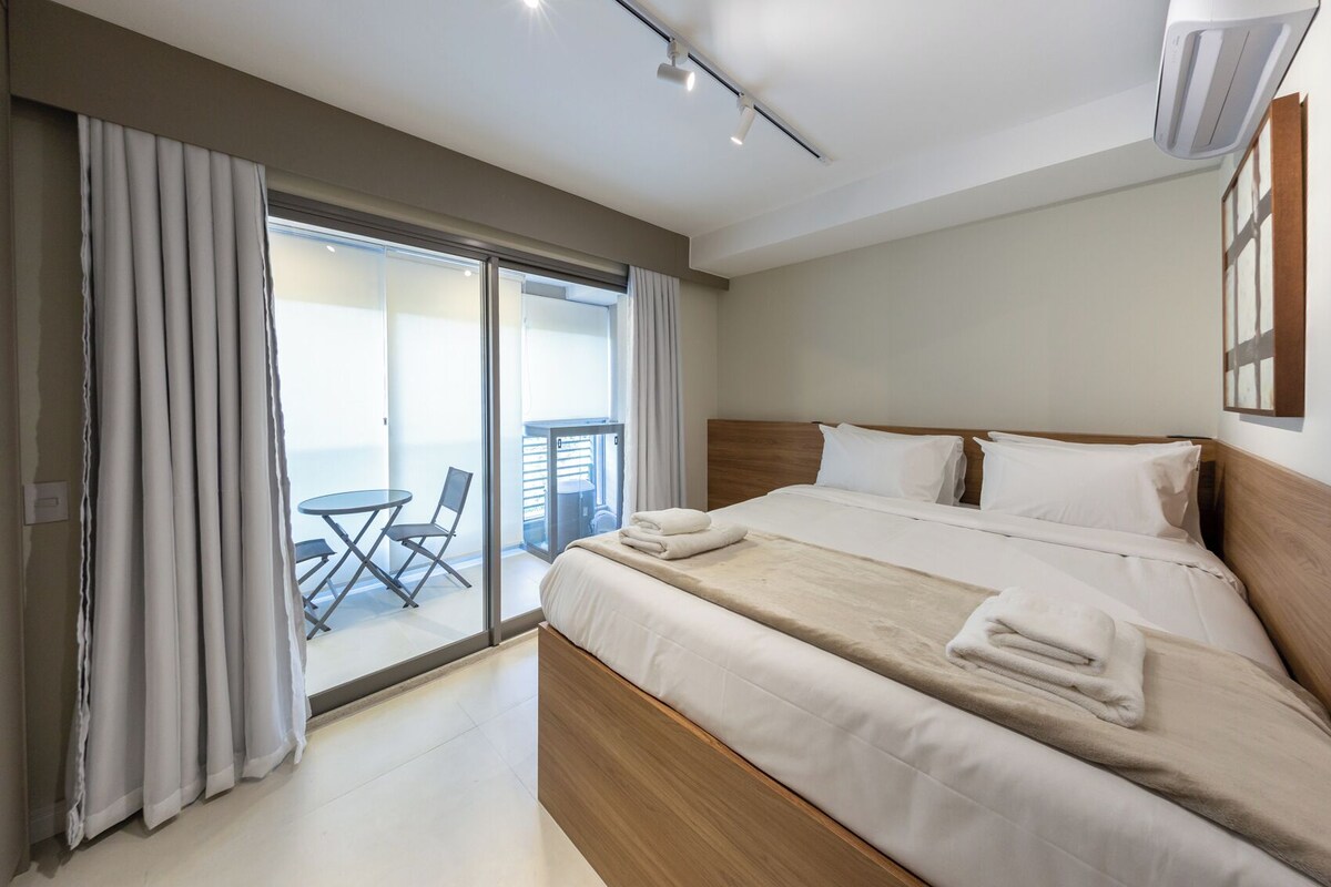 A hotel room with a bed, a balcony with a table and chairs, and a view of the outside.