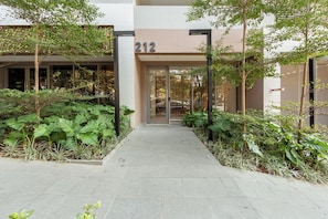 A building entrance with a number '212' above the door, surrounded by greenery and a paved walkway. - Caraibas by Bhomy (São Paulo)