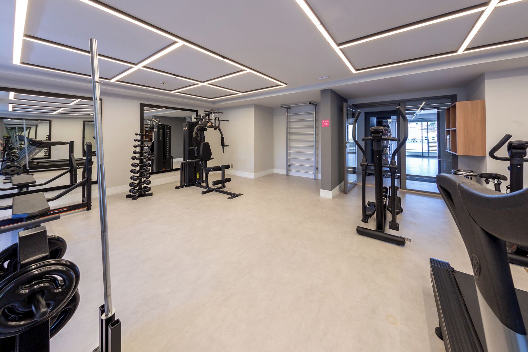 A modern gym with various exercise equipment, a mirror, and a clean, light-colored floor.