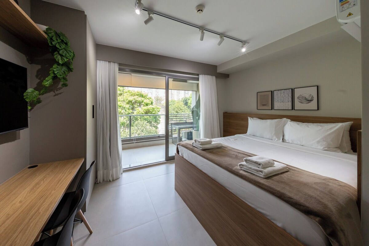A modern hotel room with a bed, a desk, and a large window.