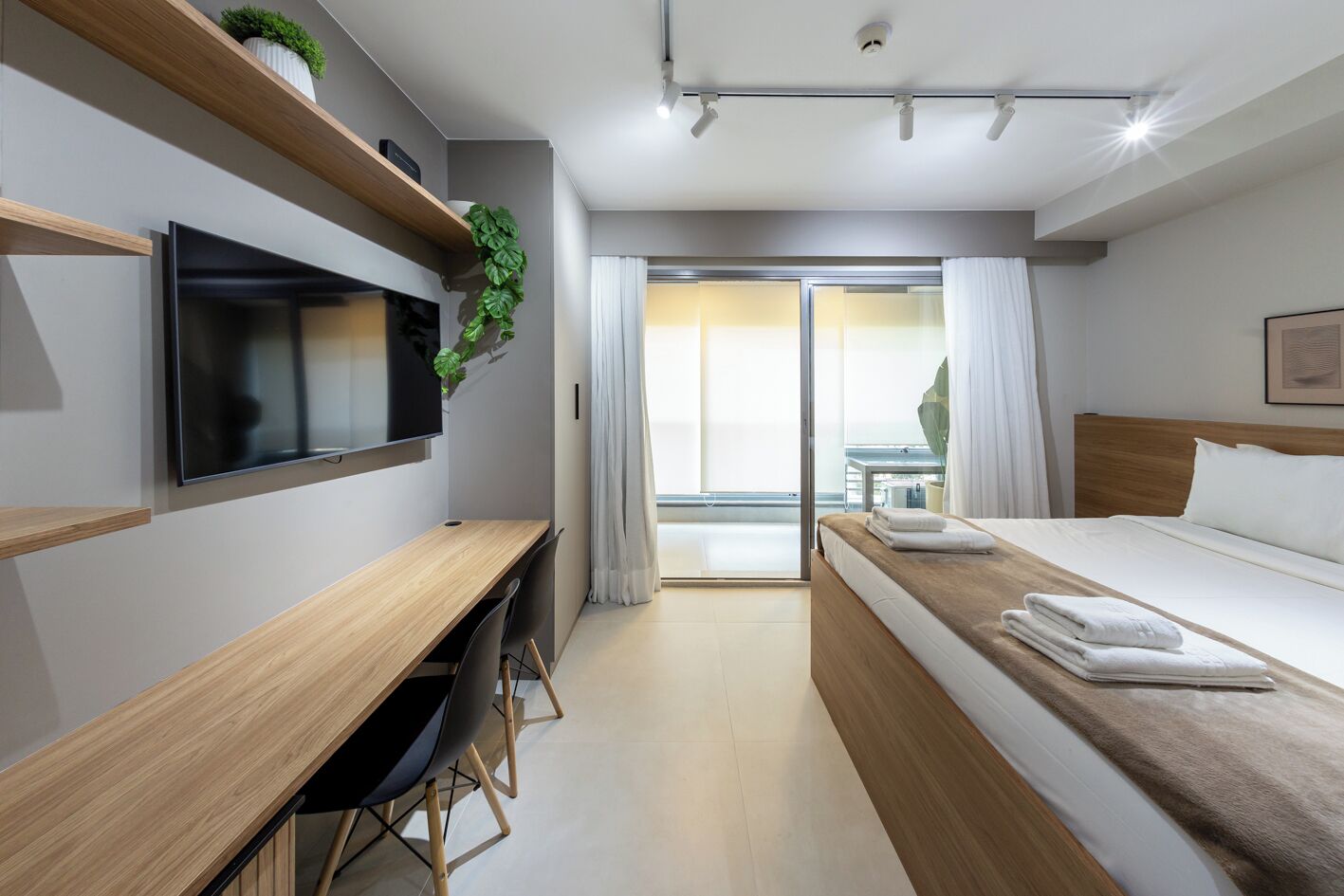 Habitación de hotel con cama, escritorio, televisión, planta y vistas al exterior.