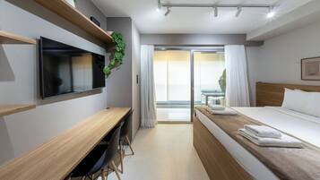 Habitación de hotel con cama, escritorio, televisión, planta y vistas al exterior.