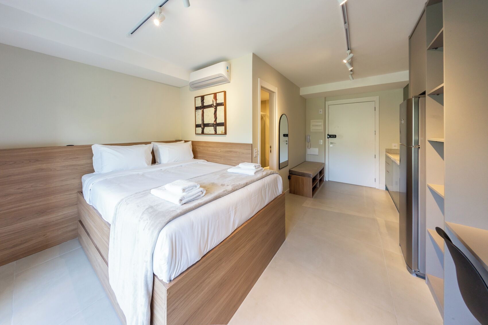 A modern hotel room with a large bed, a bedside table, a wardrobe, and a bathroom visible through an open door.