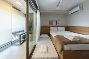 Una habitación de hotel con cama, ventana, puerta corredera y aire acondicionado.