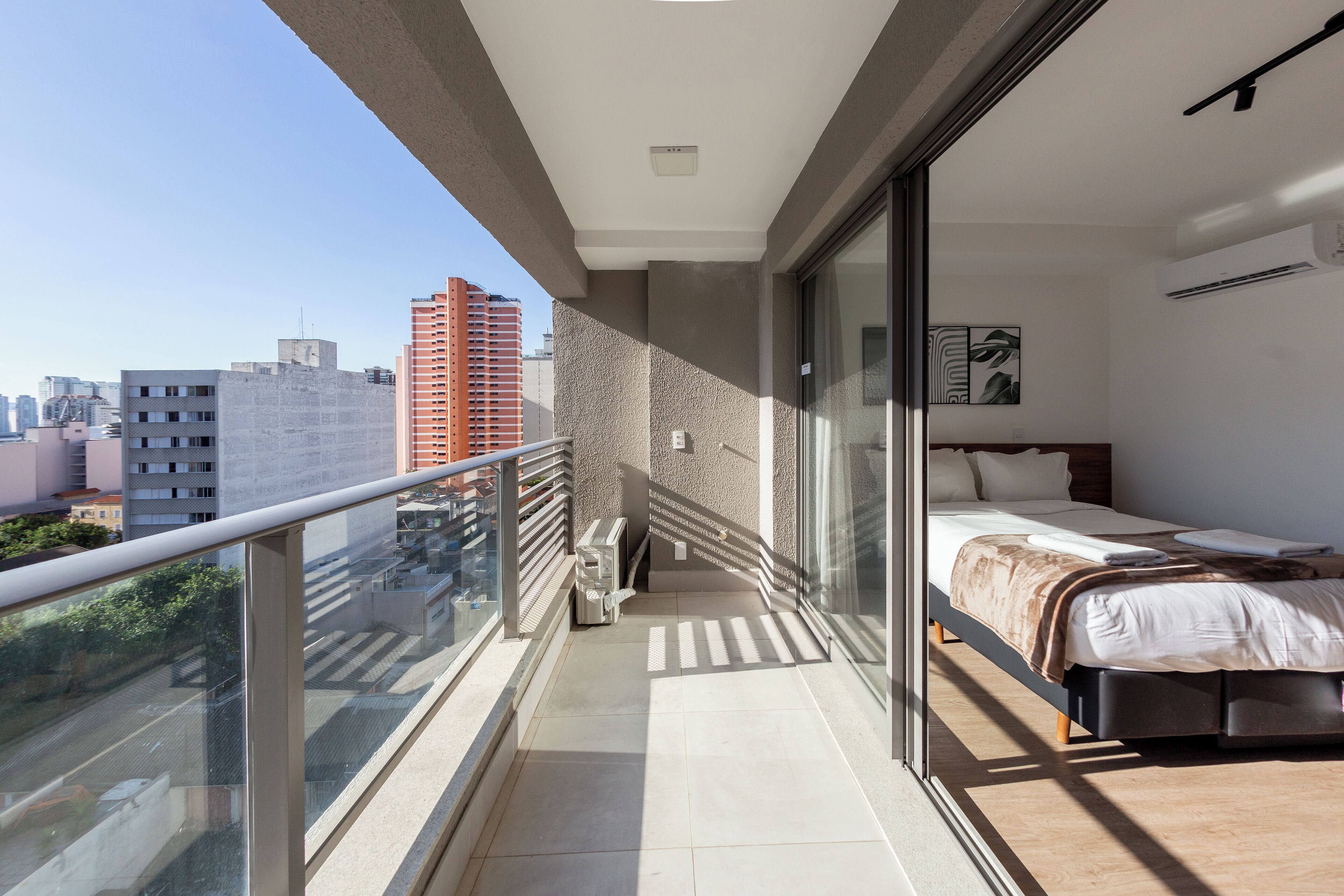 A modern bedroom with a large bed, a glass door leading to a balcony, and a city view.