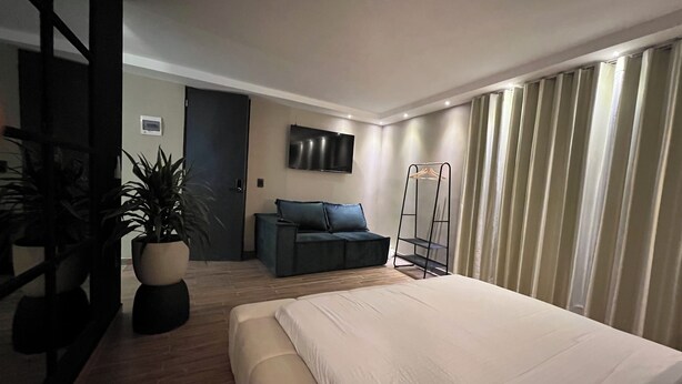 A modern hotel room with a large bed, a sofa, a TV mounted on the wall, and a plant. - Luxury Sense II (Medellín)