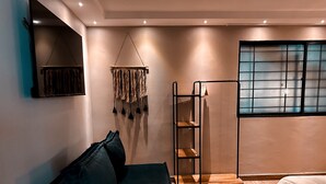 A modern bedroom with a sofa, a hanging decor, a window with a grid pattern, and a wooden floor. - Luxury Sense II (Medellín)