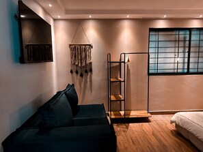 Ein modernes Schlafzimmer mit Sofa, Wanddeko, einem Fenster mit Gittermuster und Holzboden.