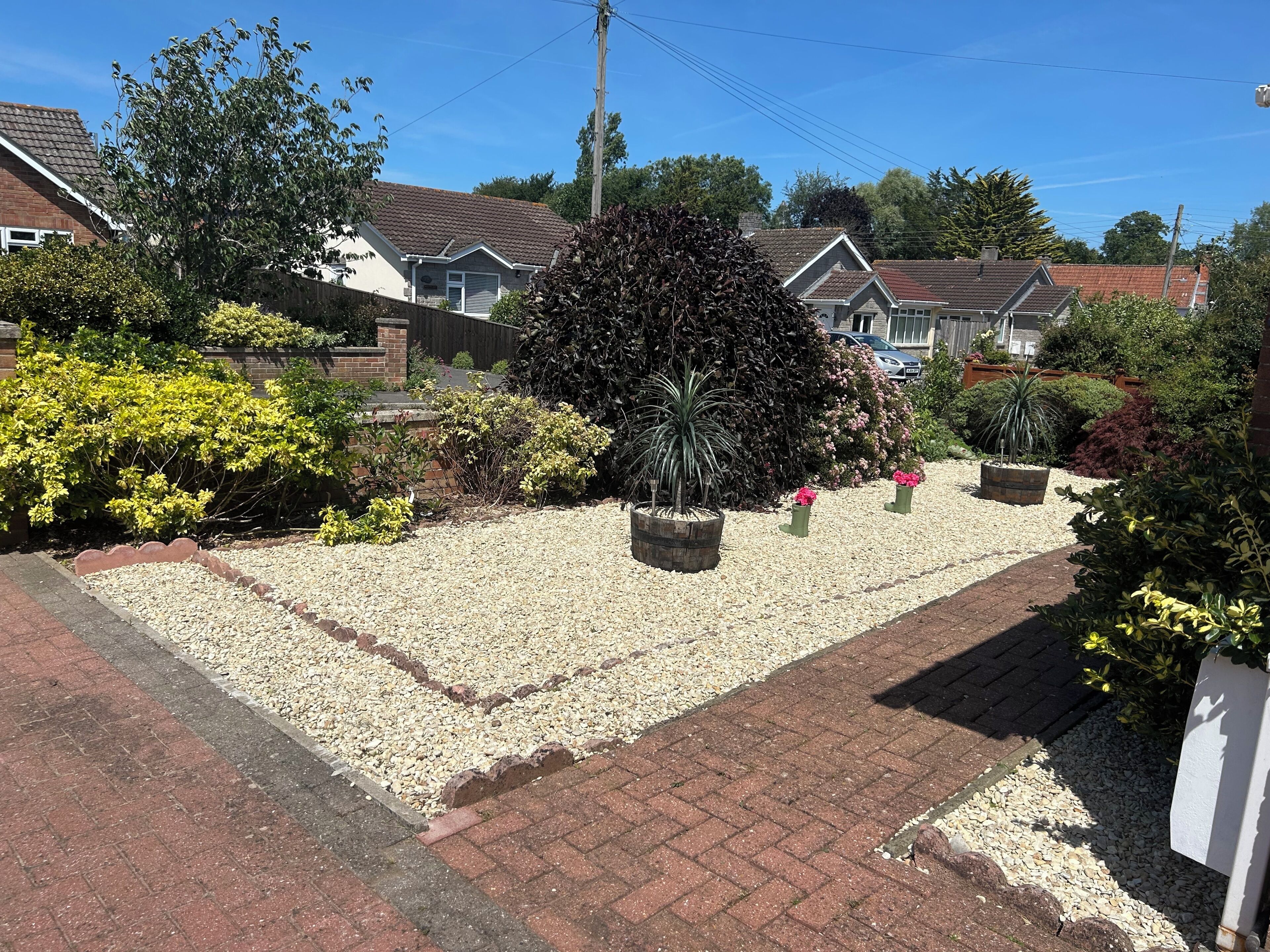 A residential garden with gravel paths, various shrubs, and potted plants.