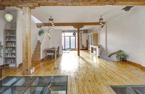 A spacious room with a wooden floor, a staircase, a dining area, and a large window. - Furnished Exec Loft | 2,200 sq ft | Short–Mid Term Rental | Rooftop Terrace (Montréal)