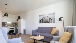 A modern living room with a sofa, two armchairs, a small coffee table, and a kitchen in the background. - Parkidylle mit Sauna (Lübeck)