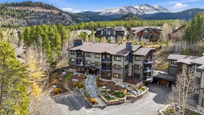 A multi-story hotel with a central courtyard, surrounded by trees and mountains in the background. - Walk to Lifts & Main St | Hot Tub (Breckenridge)