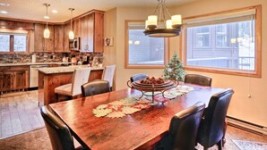 A kitchen with wooden cabinets, a central island, and a dining area with a table set for four. - Walk to Lifts & Main St | Hot Tub (Breckenridge)