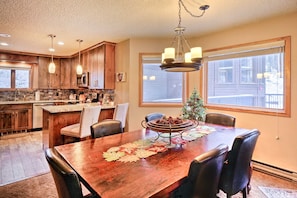 A kitchen with wooden cabinets, a central island, and a dining area with a table set for four. - Walk to Lifts & Main St | Hot Tub (Breckenridge)