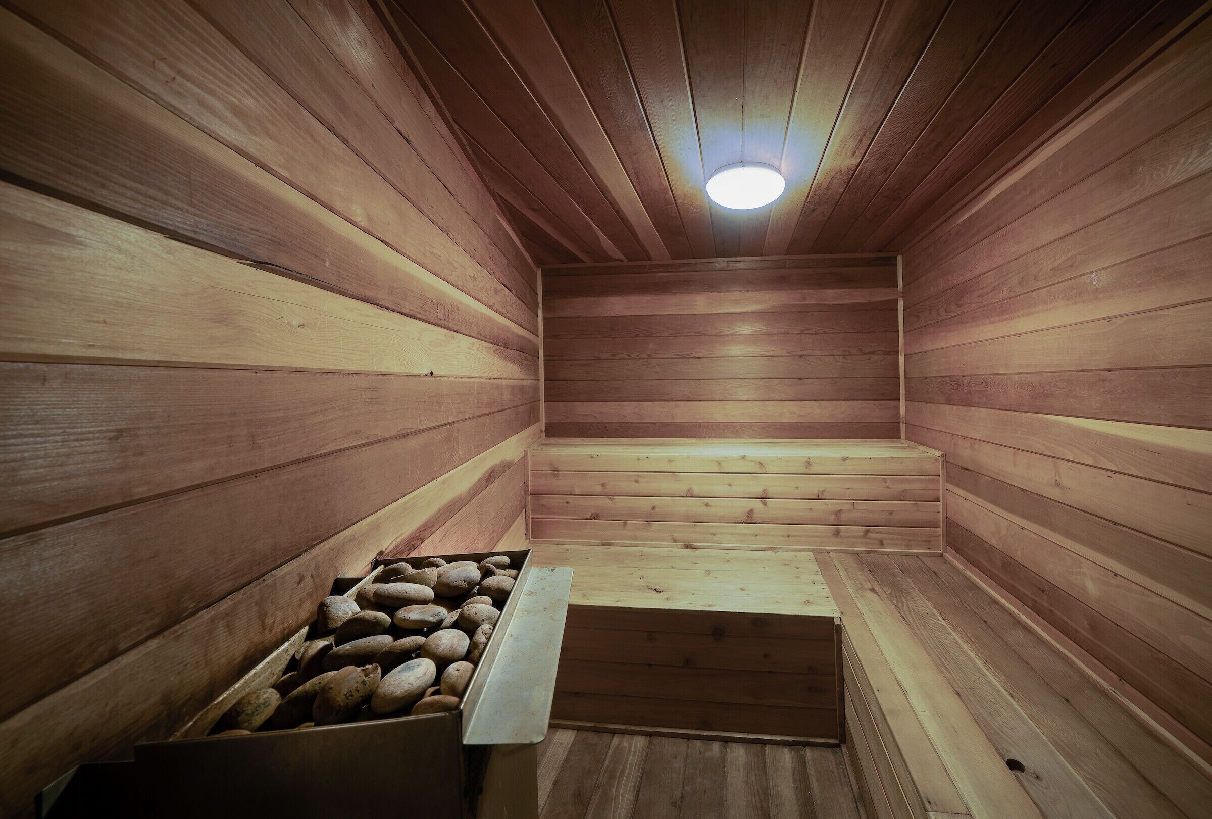Eine Holzsauna mit Bänken und einem steinbegefüllten Behälter.
