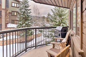 A balcony with a grill, a chair, and a view of a snow-covered landscape with trees. - Walk to Lifts & Main St | Hot Tub (Breckenridge)