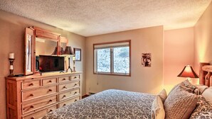 A bedroom with a bed, dresser, television, and a window with a view of snow-covered trees. - Walk to Lifts & Main St | Hot Tub (Breckenridge)
