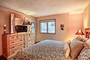 A bedroom with a bed, dresser, television, and a window with a view of snow-covered trees. - Walk to Lifts & Main St | Hot Tub (Breckenridge)