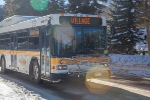 Um ônibus com a palavra 'VILLAGE' na frente, seguindo por uma estrada com neve nas laterais.