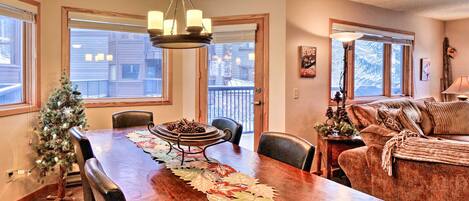 A dining area with a wooden table, chairs, a chandelier, and a Christmas tree.