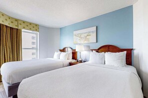 A hotel room with two beds, a window with curtains, a painting on the wall, and a nightstand with a lamp. - Carolinian Beach Resort 0933 (Myrtle Beach)