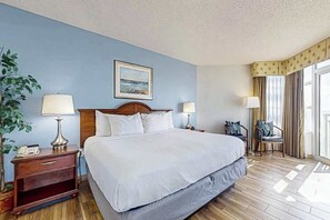 A hotel room with a bed, bedside lamps, a nightstand, a chair, a window with curtains, and a wall-mounted painting. - Carolinian Beach Resort 0933 (Myrtle Beach)