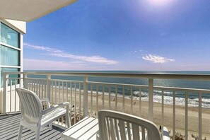 A balcony with white chairs and a table overlooking a beach with a clear sky. - Carolinian Beach Resort 0933 (Myrtle Beach)