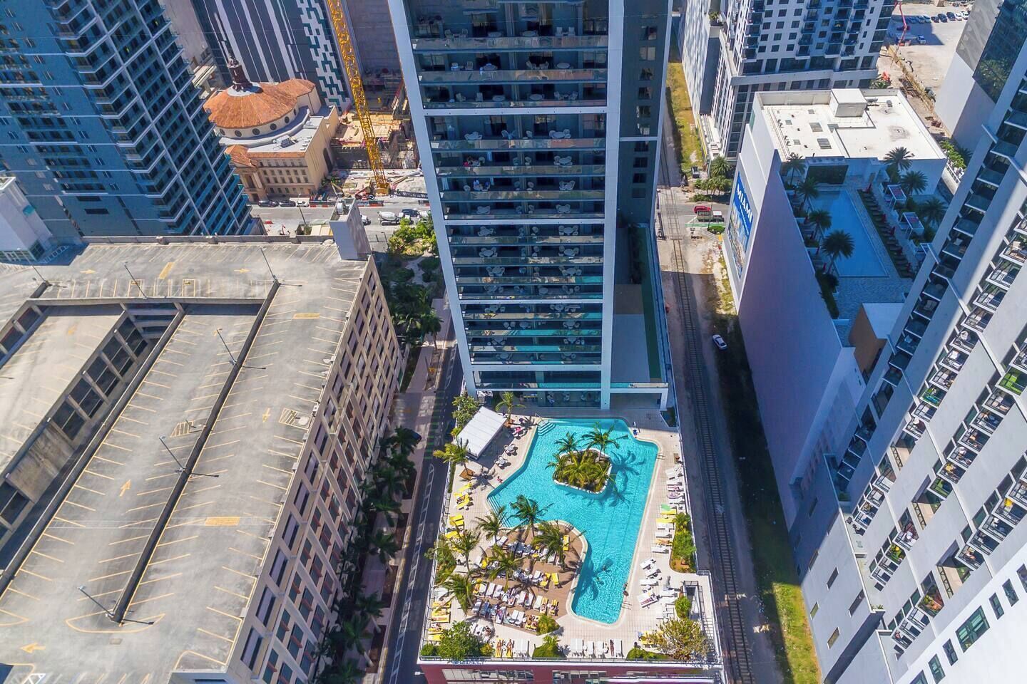 A high-rise building with a rooftop pool surrounded by palm trees and lounge chairs.