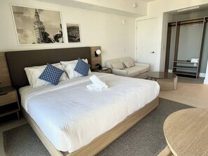 Et hotelværelse med en stor seng, et natbord, en stol, et lille rundt bord og et klædeskab.