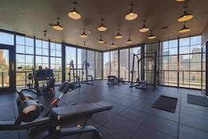 A gym with various exercise equipment, large windows, and a city view. - Modern Studio with Balcony in Downtown Miami (Miami)
