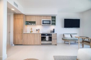 A modern kitchen with wooden cabinets, a microwave, and a built-in oven. There is a dining area with a table and chairs, and a flat-screen TV mounted on the wall. - Modern Studio with Balcony in Downtown Miami (Miami)